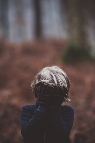 Blonde boy with hands covering his face in forest
